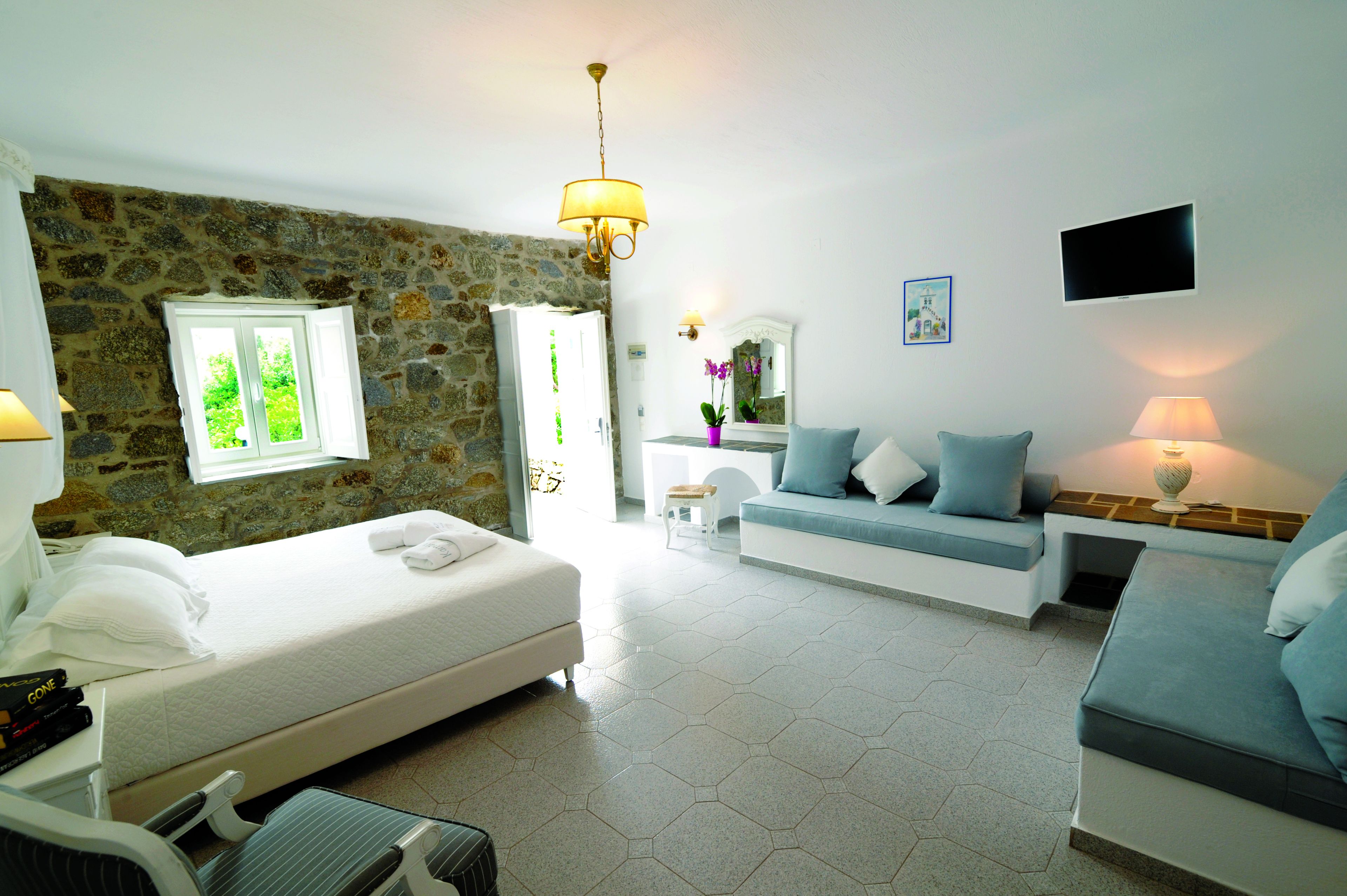 Een moderne hotelkamer met een stenen muur, een bed, een sofa, een televisie en een klein tafeltje met een lamp.