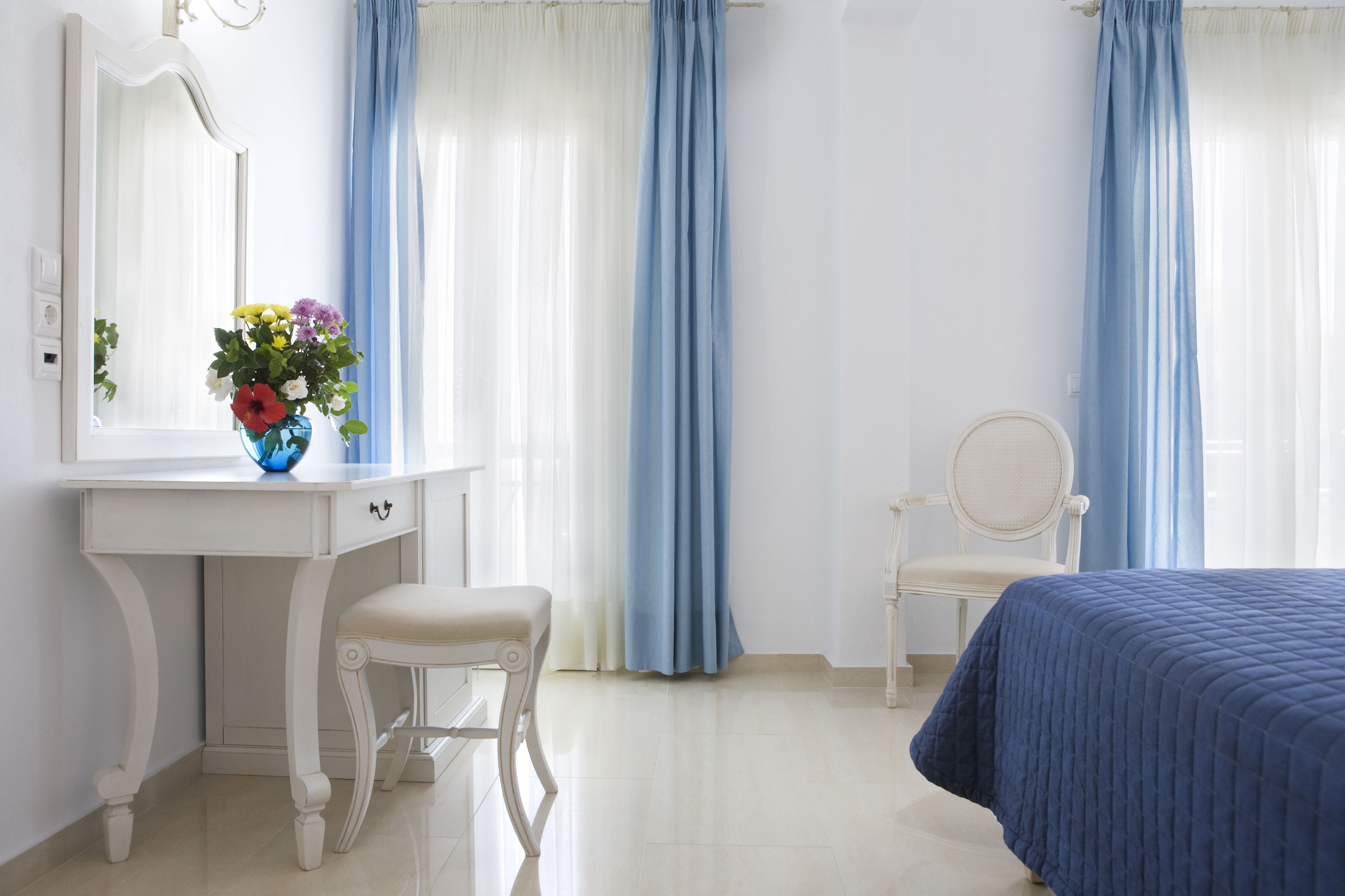 A bedroom with a bed, a vanity with a mirror, a chair, and a vase of flowers.
