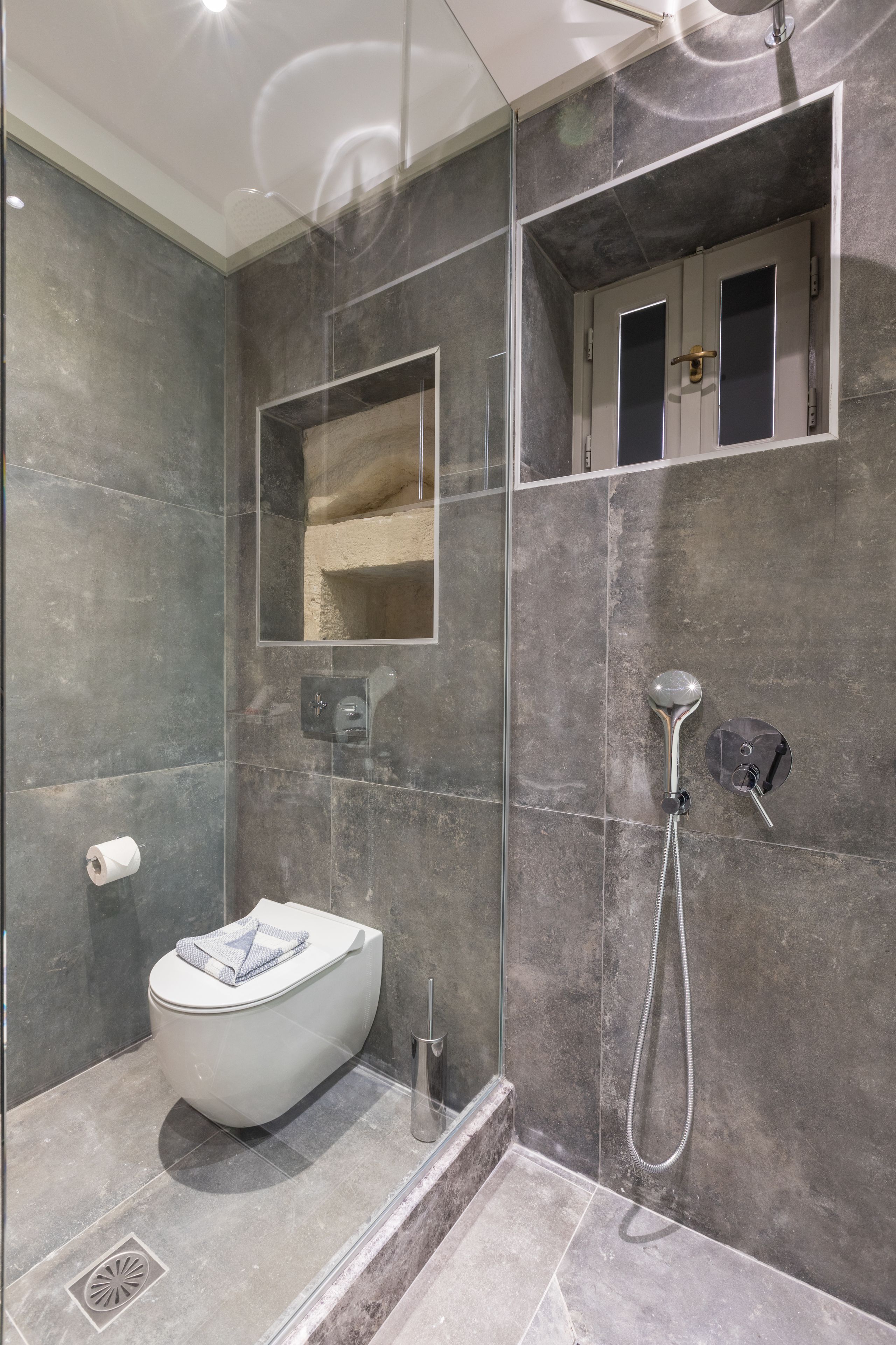 A modern bathroom with a glass-enclosed shower, a white toilet, and a built-in mirror.