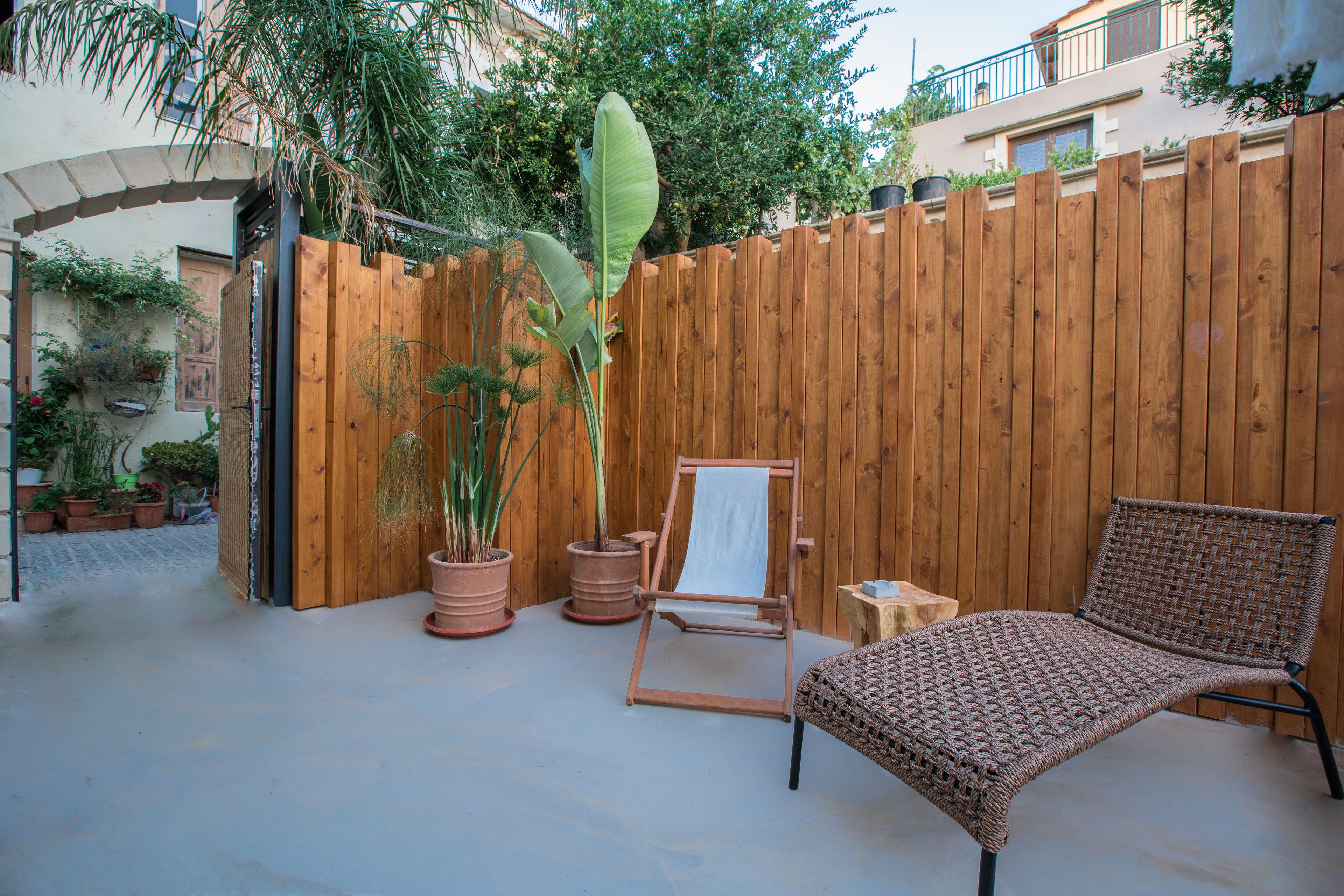 A wooden fence, a wicker chair, and a canvas easel in a courtyard with potted plants.