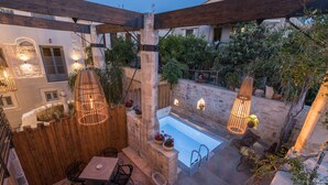 Een terras buiten met een zwembad, een houten pergola en een zithoek.