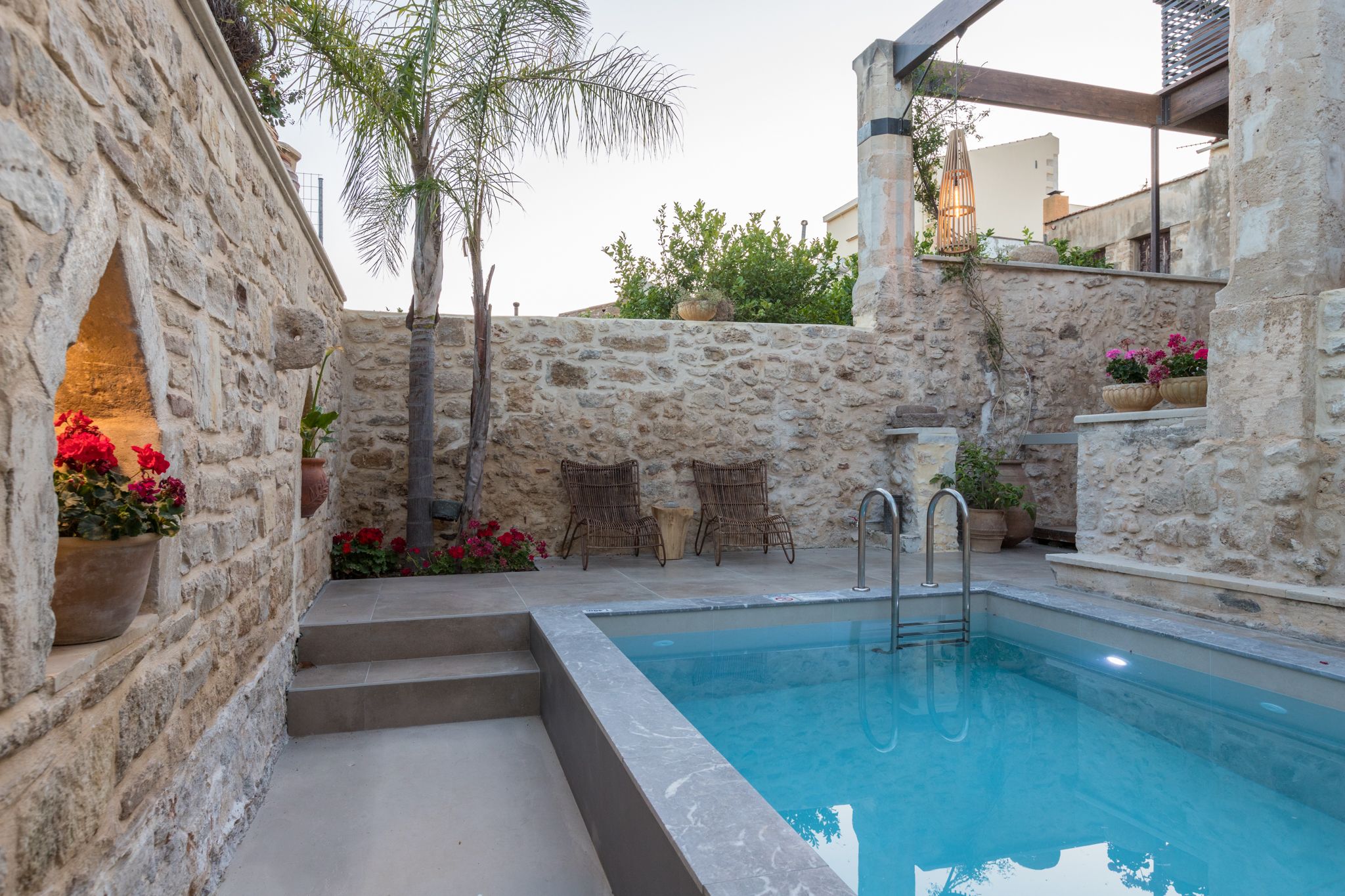 A stone-walled pool area with steps leading to the pool, wicker chairs, and potted plants.