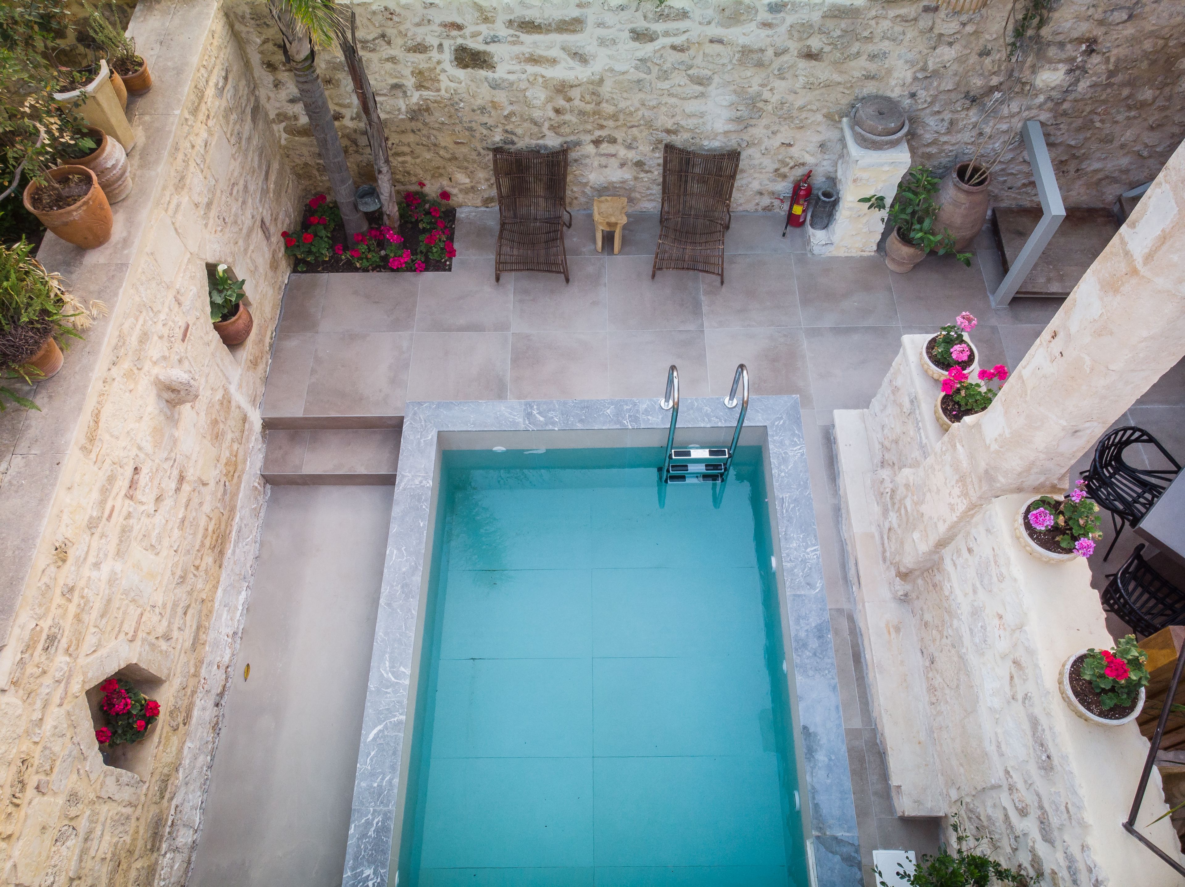 A rooftop pool with a stone wall and potted plants around it.