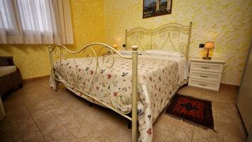 Um quarto com estrutura de cama de metal, uma mesa de cabeceira com abajur e um tapete estampado.