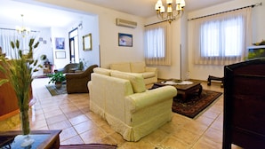 A living room with a sofa, a coffee table, and a TV. There is a chandelier, a potted plant, and a rug. - Hotel History (Valderice)
