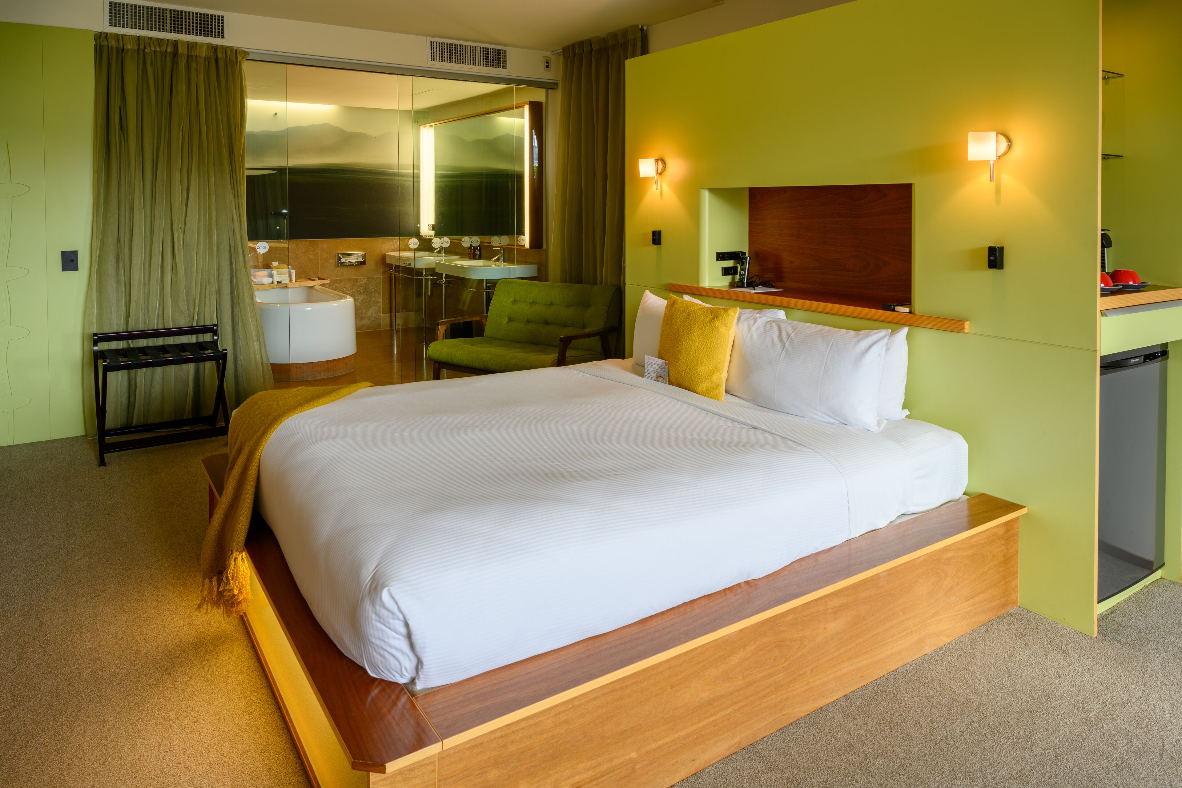 A hotel room with a large bed, a desk, a chair, a small table, a mirror, and a bathroom.