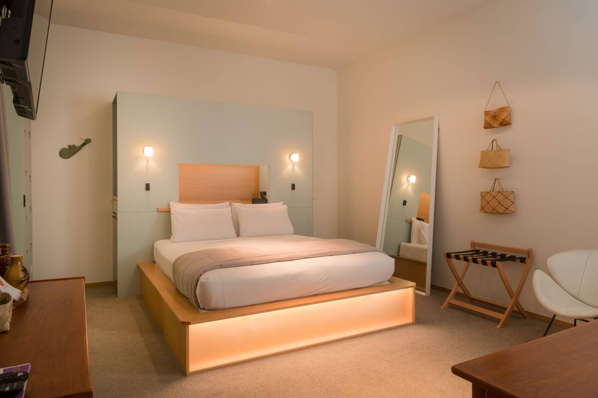 A modern bedroom with a wooden bed frame, bedside lamps, a small wooden chair, and a mirror on the wall.