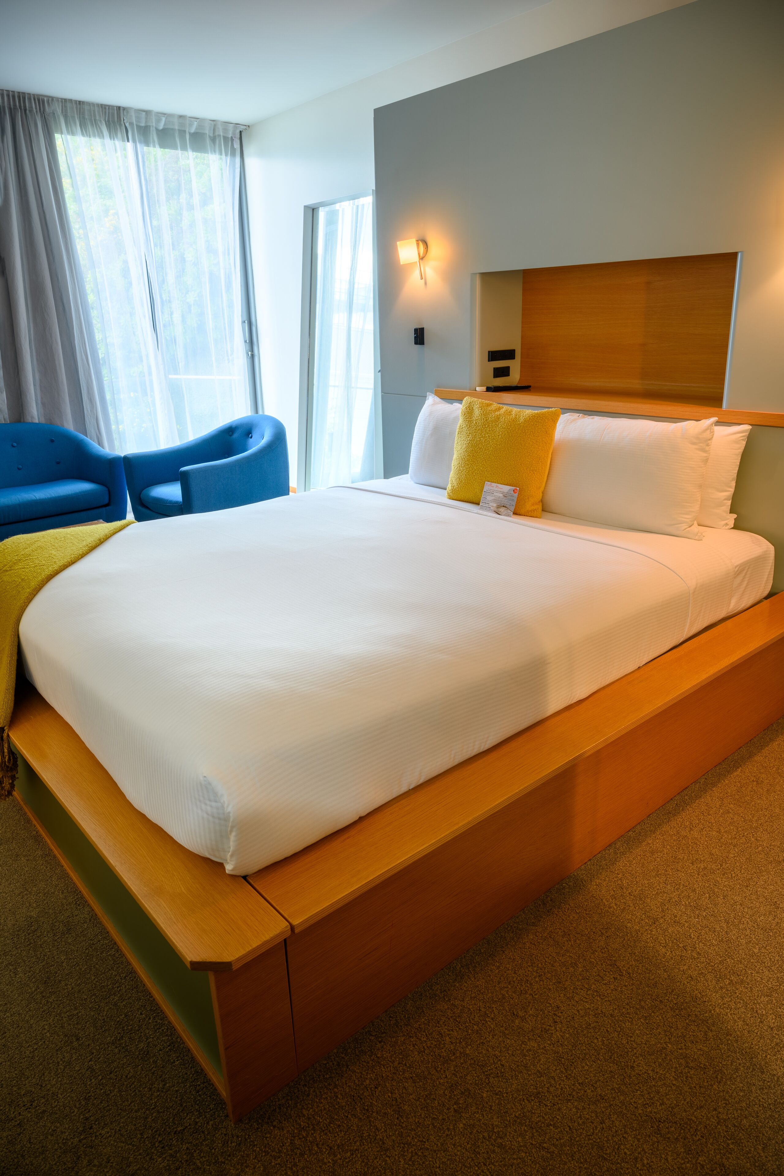 A hotel room with a large bed, wooden headboard, and a seating area with blue chairs.