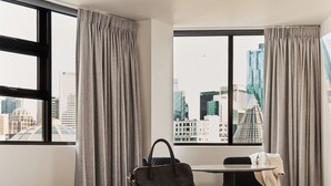 A hotel room with a large bed, a desk, and a view of the cityscape through large windows. - Space Hotel - Hostel (Melbourne)