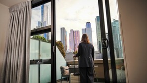 A hotel room with a large window, a bed, a chair, and a suitcase. - Space Hotel - Hostel (Melbourne)