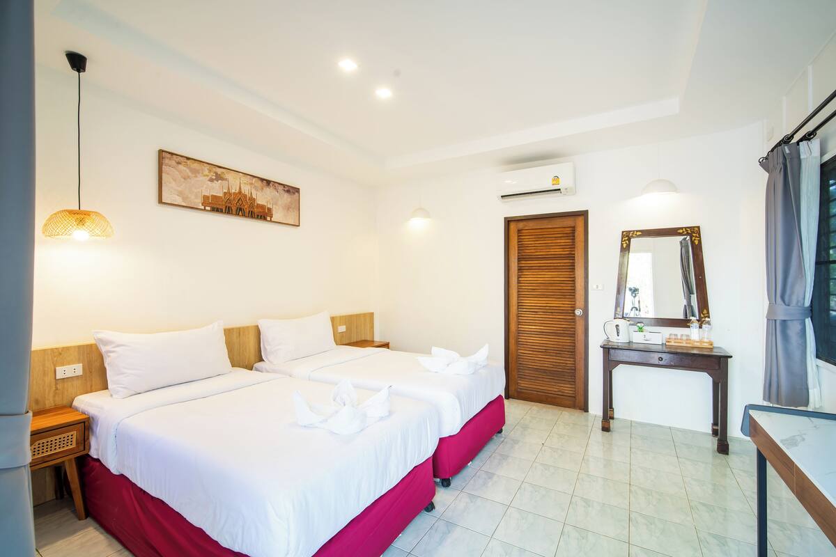 A hotel room with two beds, a wooden nightstand, a desk with a mirror, and a wall-mounted air conditioner.