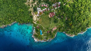An aerial view of a coastal property with a swimming pool, multiple buildings, and lush greenery.