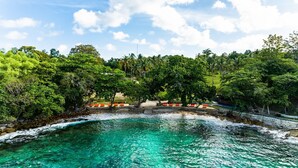 A coastal area with clear turquoise waters, a stone pathway leading to a beach, and lush green trees. - Ban Raya Resort and Spa (Ko Racha Yai)