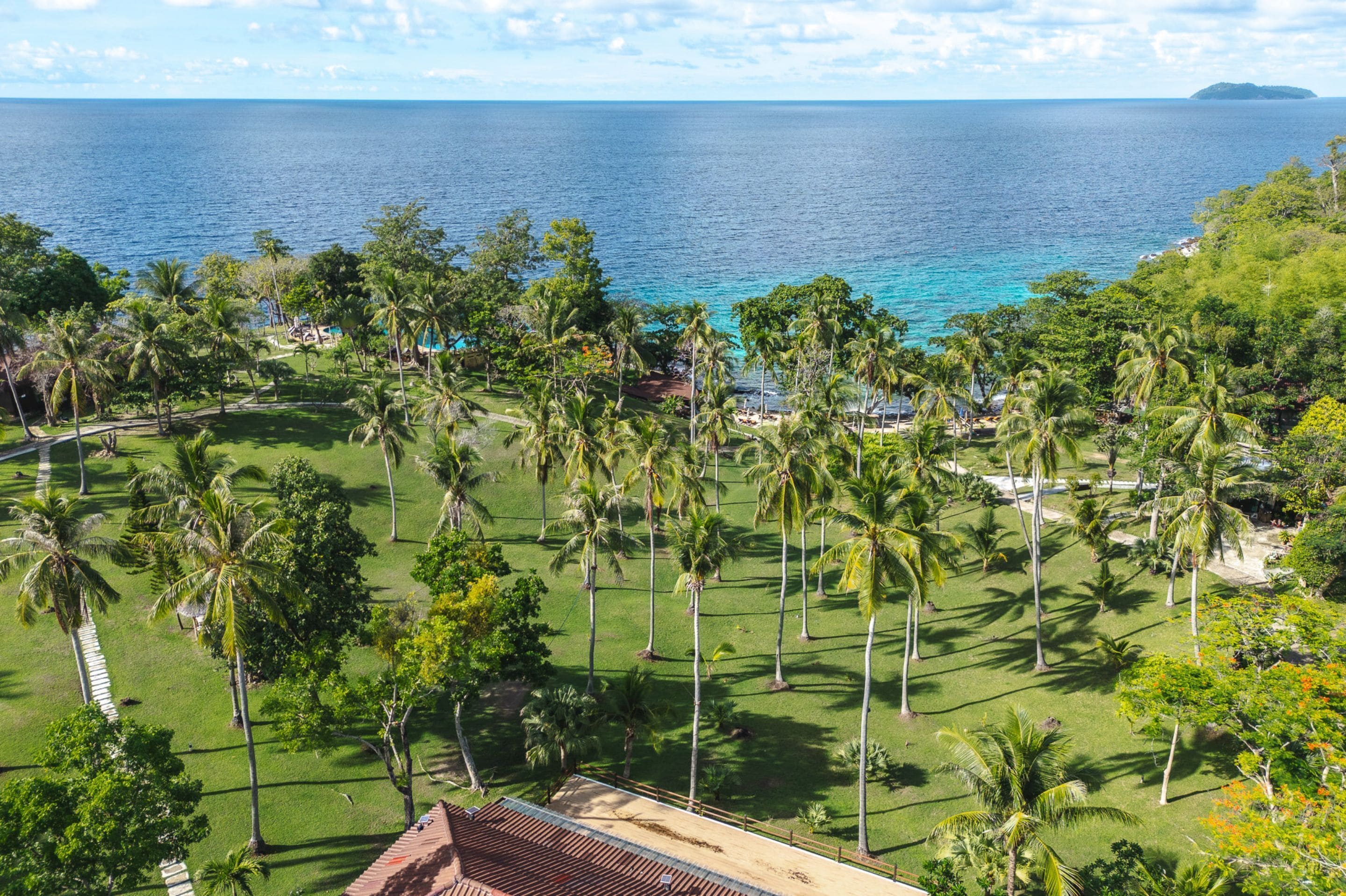 A tropical resort with a view of the ocean, palm trees, and a well-maintained lawn.