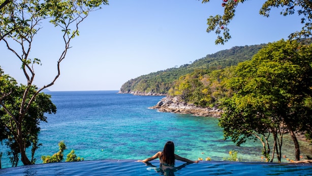 A woman relaxing in a clear blue infinity pool with a view of the ocean and a forested hillside. - Ban Raya Resort and Spa (Ko Racha Yai)