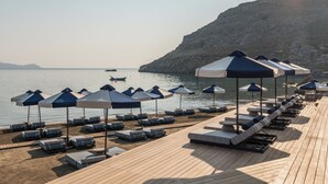 Una terraza de madera con sillones de descanso y sombrillas, con vista a un agua tranquila y un paisaje montañoso.