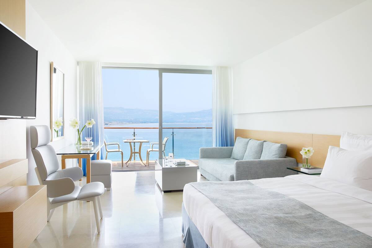 Una habitación de hotel moderna con una cama grande, un sofá, un escritorio con una silla y un balcón con vista al mar.