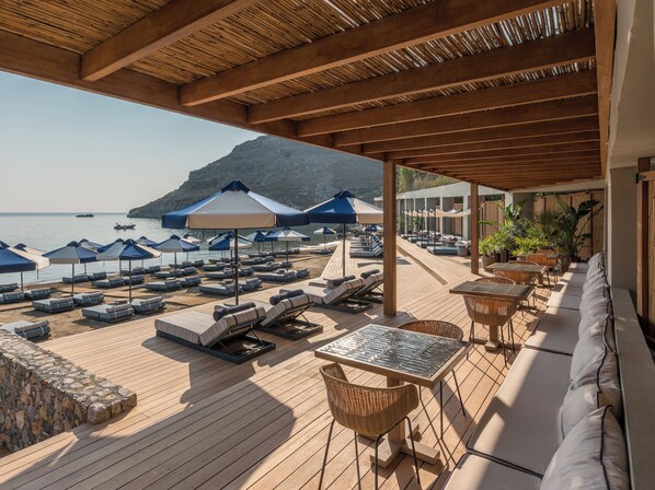 Une terrasse en bois avec des chaises longues et des parasols, donnant sur une plage.