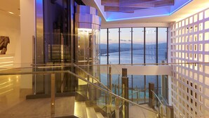 Un interior moderno con una escalera de cristal, vigas de madera en el techo y vistas al mar.