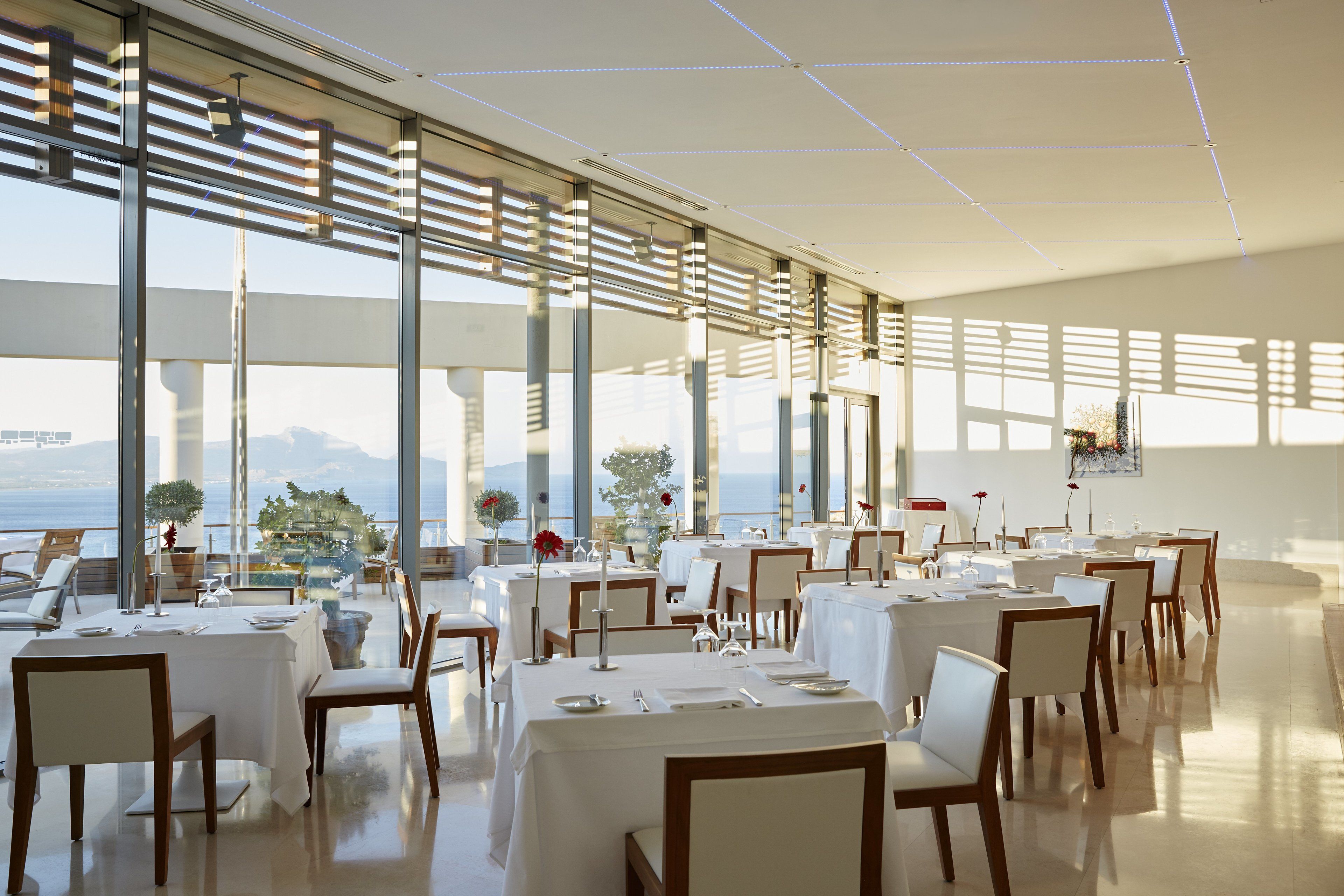 A spacious dining area with tables set for multiple guests, large windows offering a view of the sea, and modern interior design.