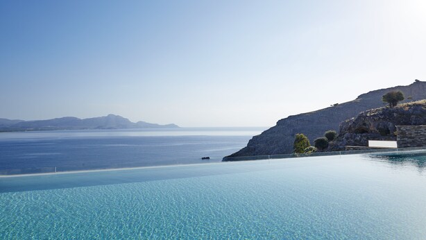 Una piscina infinita de aguas cristalinas con vista al mar y montañas lejanas.