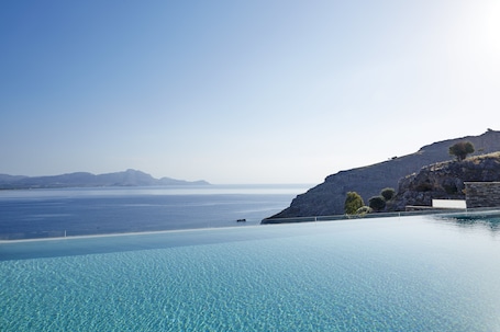 A clear blue infinity pool with a view of the sea and distant mountains.
