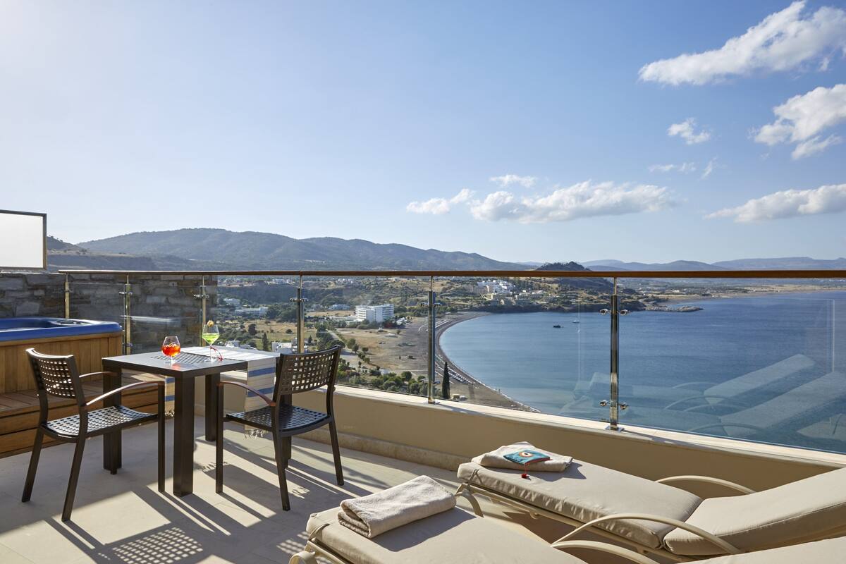 Un balcón con mesa, sillas y sofá que da a vistas costeras con montañas al fondo.