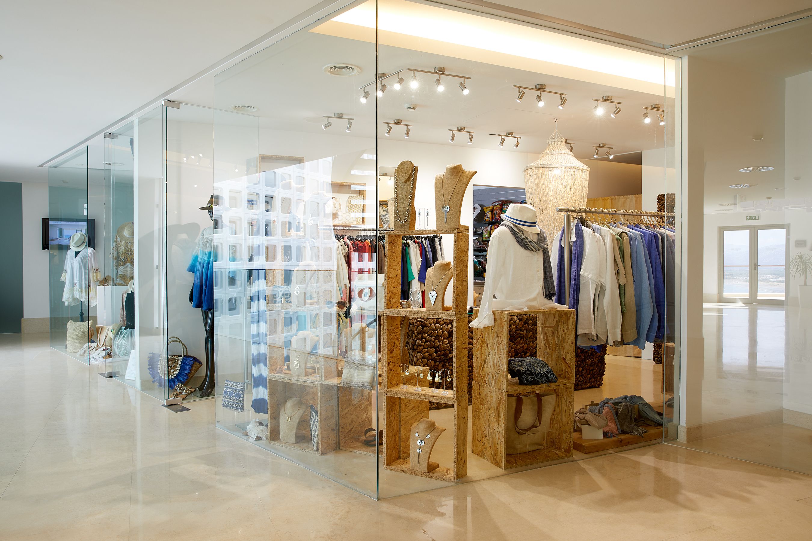 A modern boutique with glass display cases and wooden shelves, featuring clothing and accessories.