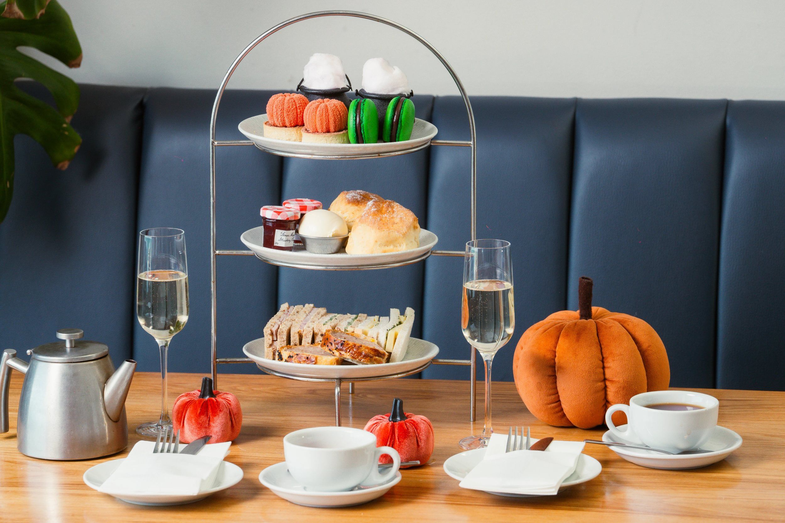 Un présentoir à trois niveaux garni de pâtisseries, une théière en métal, des tasses de café et une citrouille décorative.