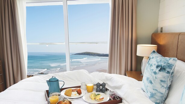A hotel room with a bed, a tray with breakfast items, a view of the ocean, and a nightstand with a lamp. - The Esplanade Hotel (Newquay)