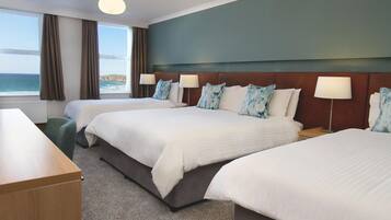 A hotel room with two beds, a desk, and a view of the sea.