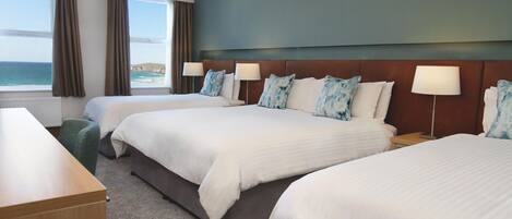 A hotel room with two beds, a desk, and a view of the sea.