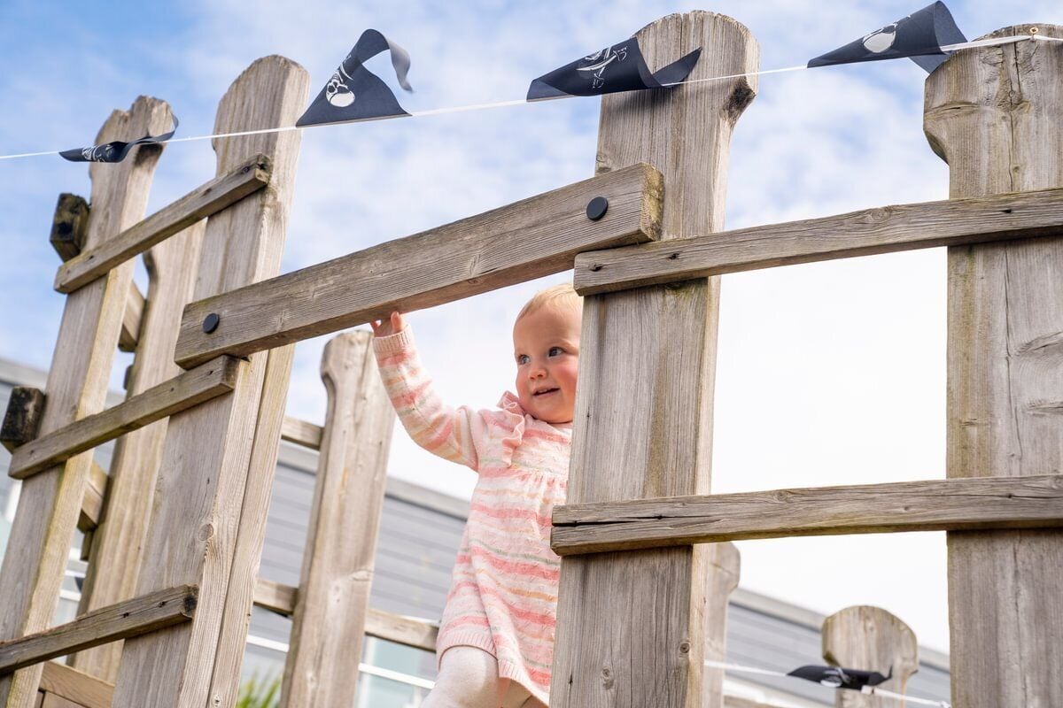 A child climbing a wooden fence with a string of flags.