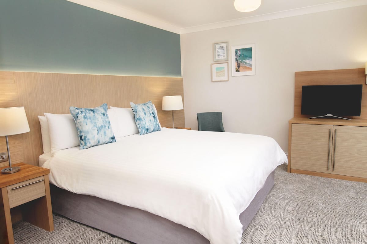 A hotel room with a large bed, two bedside tables with lamps, a flat-screen TV, and a wooden cabinet.