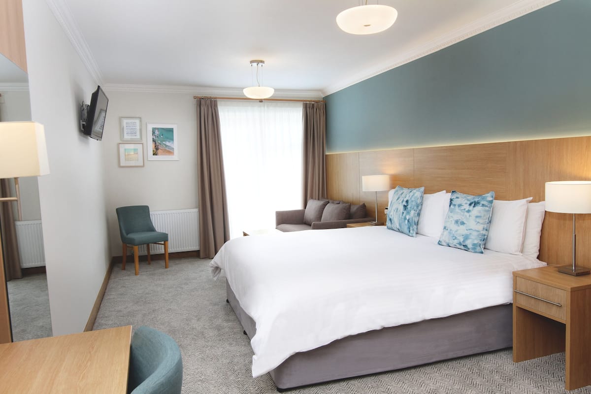 A hotel room with a large bed, a desk, a chair, a sofa, and a TV mounted on the wall.