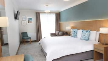 A hotel room with a large bed, a desk, a chair, a sofa, and a TV mounted on the wall.