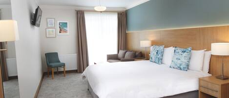A hotel room with a large bed, a desk, a chair, a sofa, and a TV mounted on the wall.
