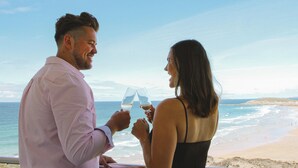 A couple toasting with wine glasses overlooking a beach with a distant bridge. - The Esplanade Hotel (Newquay)