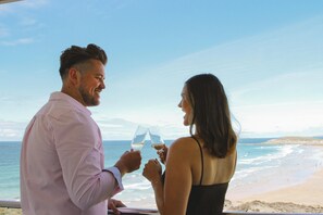 A couple toasting with wine glasses overlooking a beach with a distant bridge. - The Esplanade Hotel (Newquay)