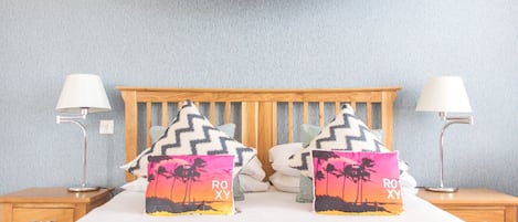 A bed with two pillows, two bedside lamps, and a surfboard decoration on the wall.