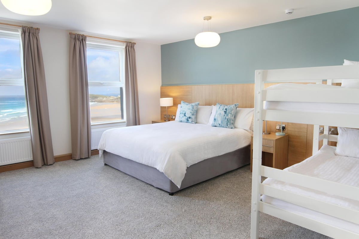 A hotel room with a large bed, a view of the beach, and a bunk bed.