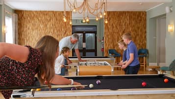 Une table de billard avec des billes, une table de baby-foot et une pancarte sur laquelle on peut lire : « LA PLAGE EST NOTRE TERRAIN DE JEU ».