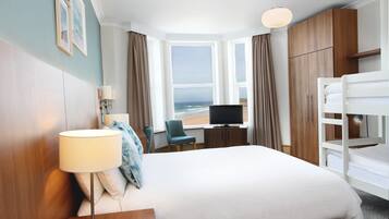 Habitación de hotel con cama, escritorio, televisor, silla y vista al océano.