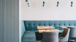 A modern interior with a teal upholstered bench, wooden tables, and grey upholstered chairs. - The Esplanade Hotel (Newquay)
