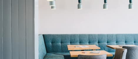 A modern interior with a teal upholstered bench, wooden tables, and grey upholstered chairs.