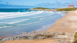 A beach with waves, a rocky shoreline, and a large building in the background. - The Esplanade Hotel (Newquay)