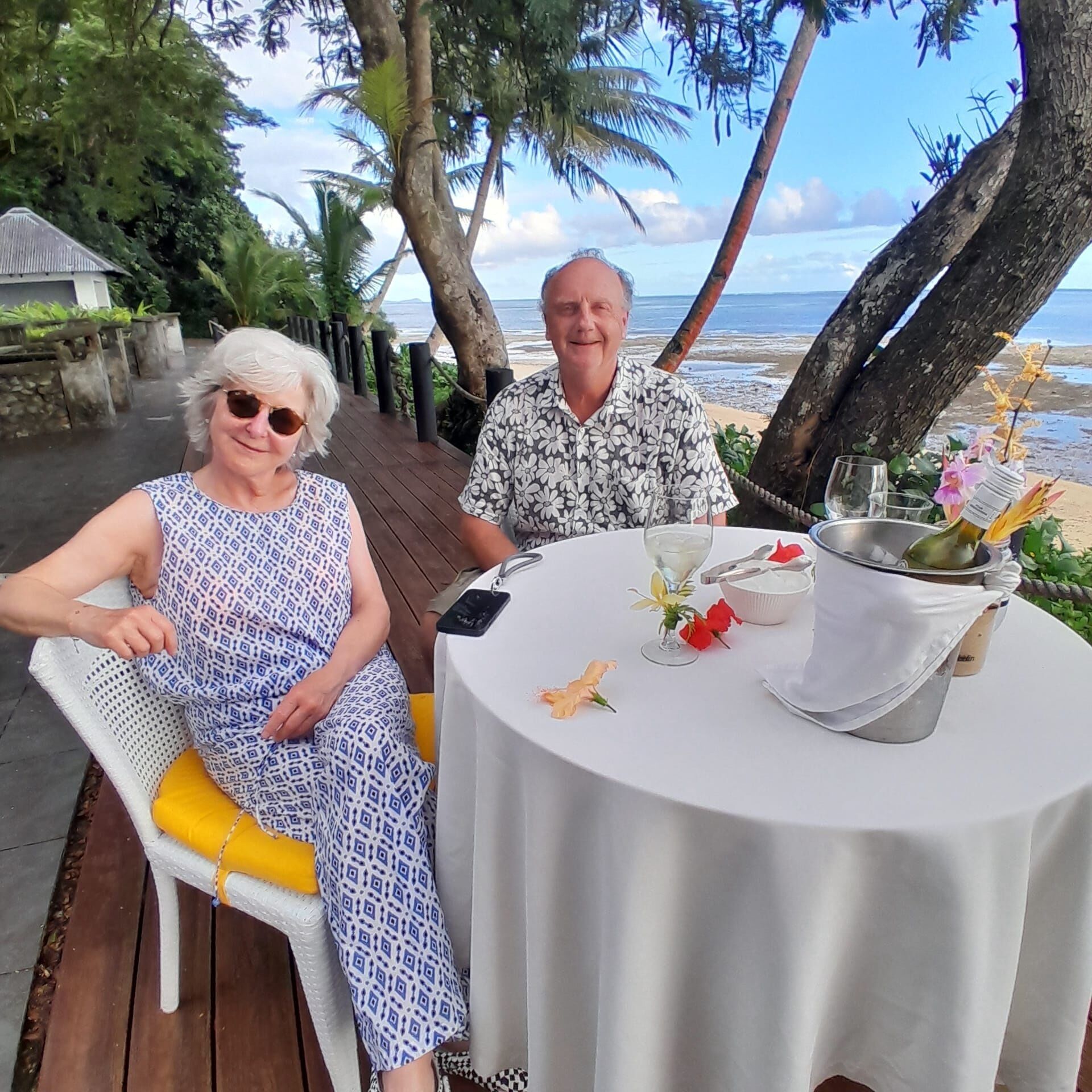 A couple seated at an outdoor table with a view of the beach and ocean.
