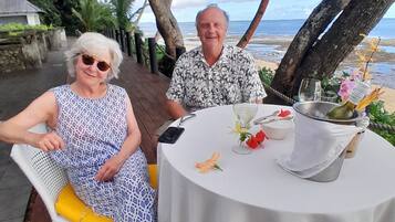 A couple seated at an outdoor table with a view of the beach and ocean.
