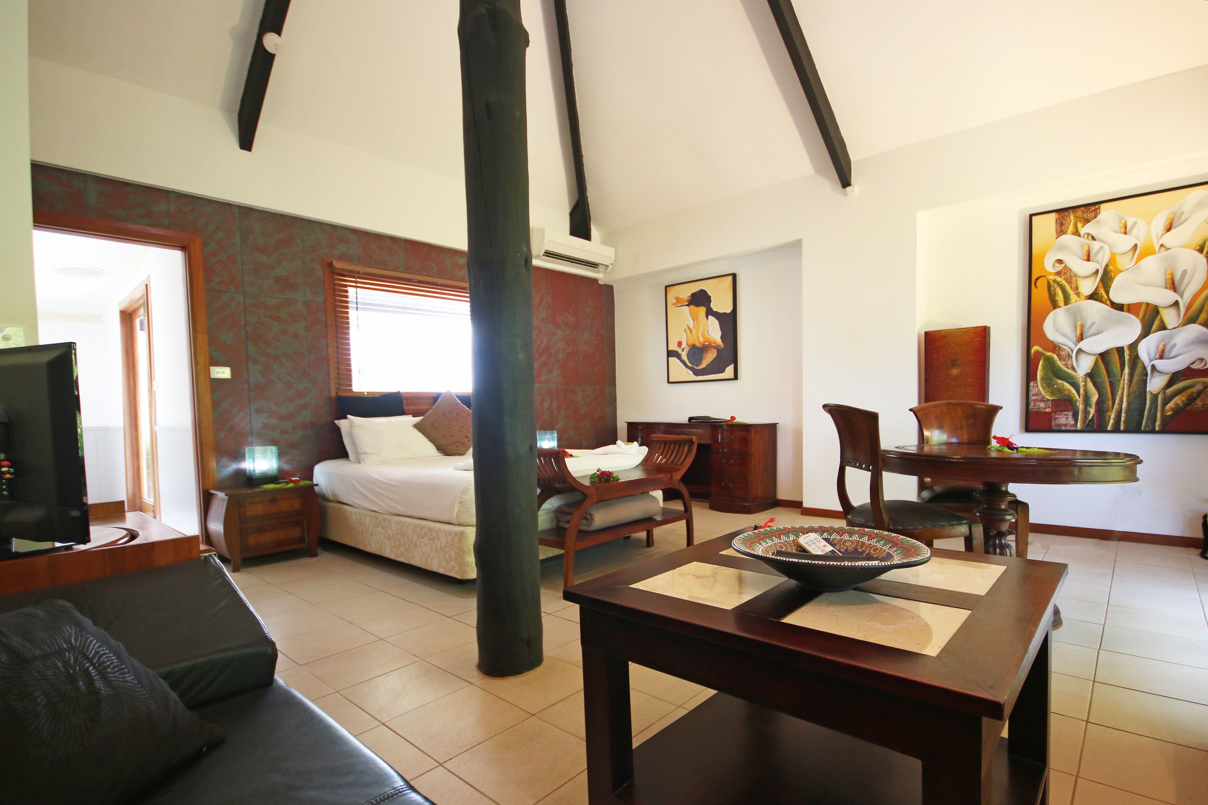 A hotel room with a bed, a sofa, a dining table, and a TV.