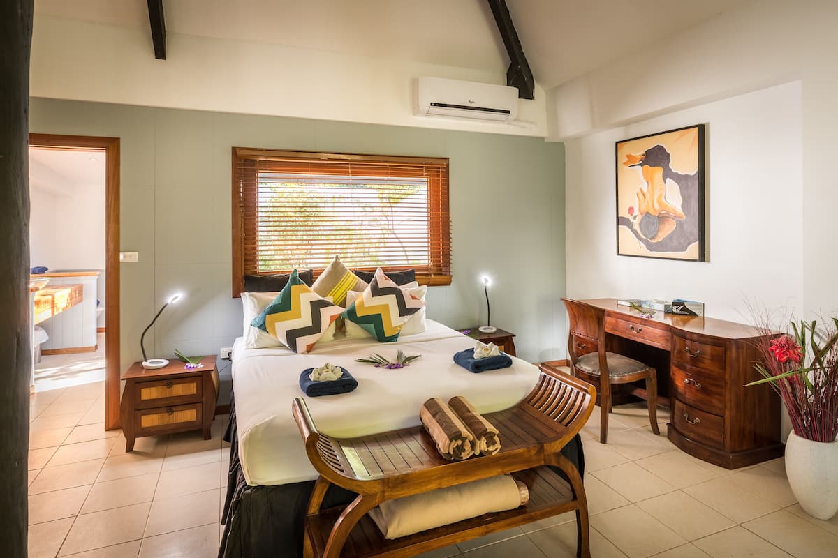 Une chambre d’hôtel comprenant un lit, des tables de chevet, un bureau, une chaise et une grande fenêtre avec des stores.